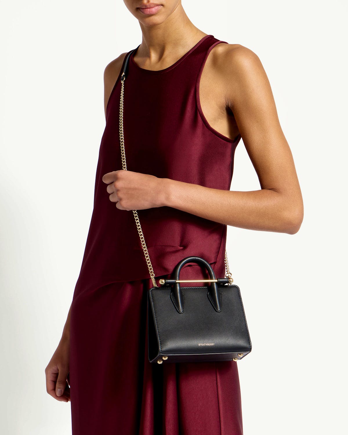 Strathberry black nano tote worn crossbody by model in burgundy dress