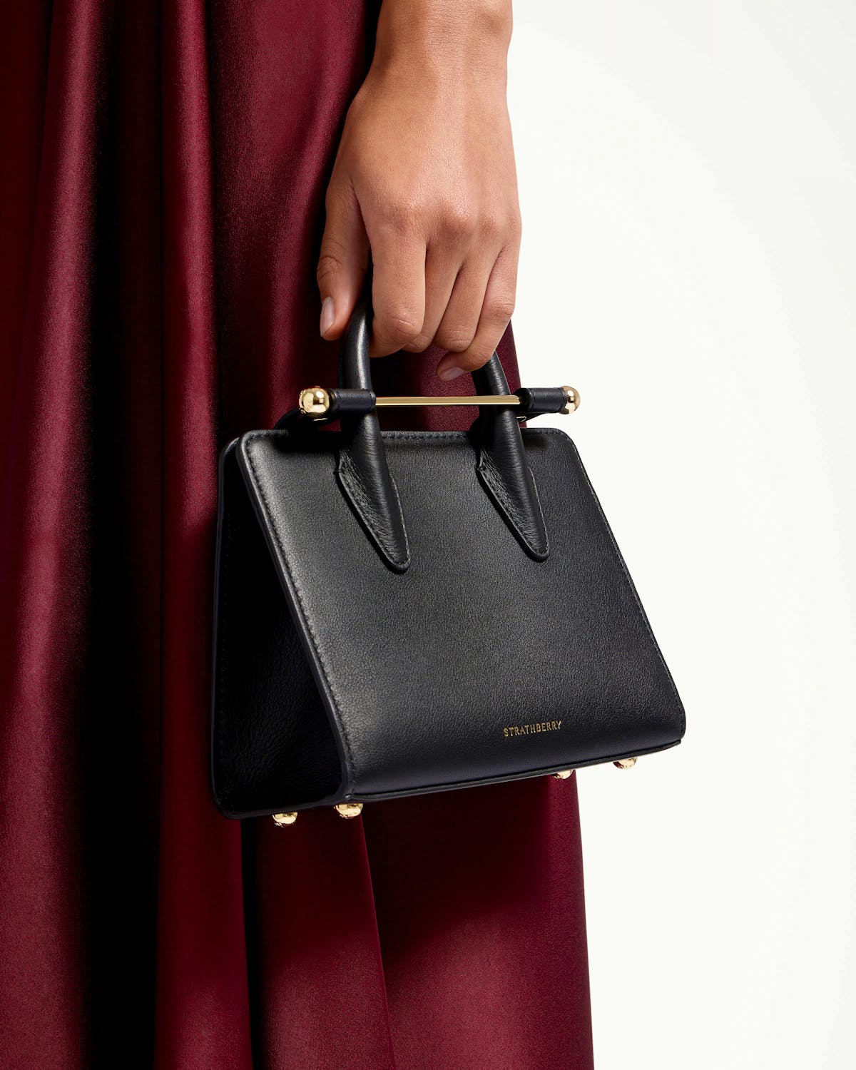 Black Strathberry nano tote held by top handles with gold bar