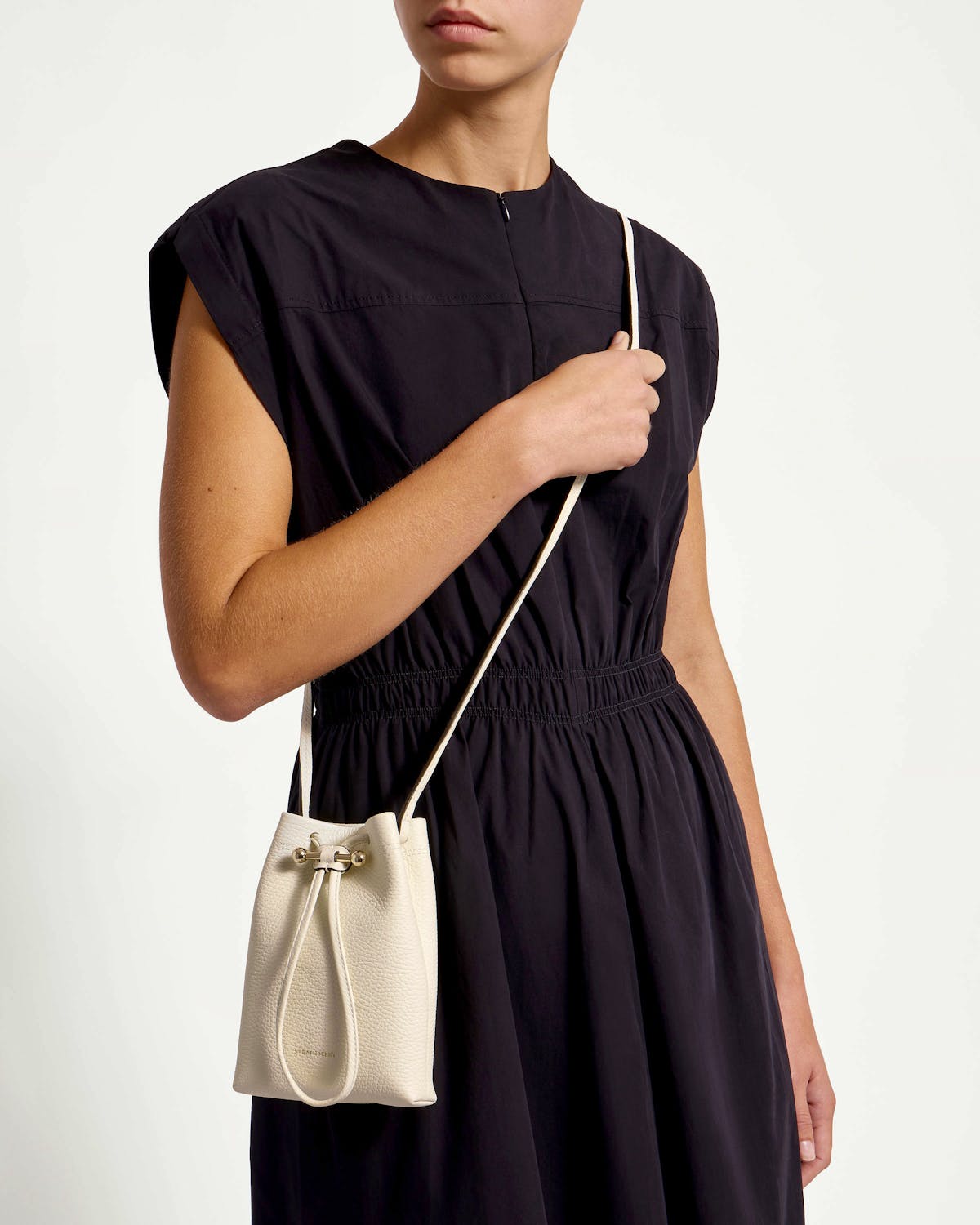 Model in black dress holding small vanilla leather drawstring midi pouch worn crossbody
