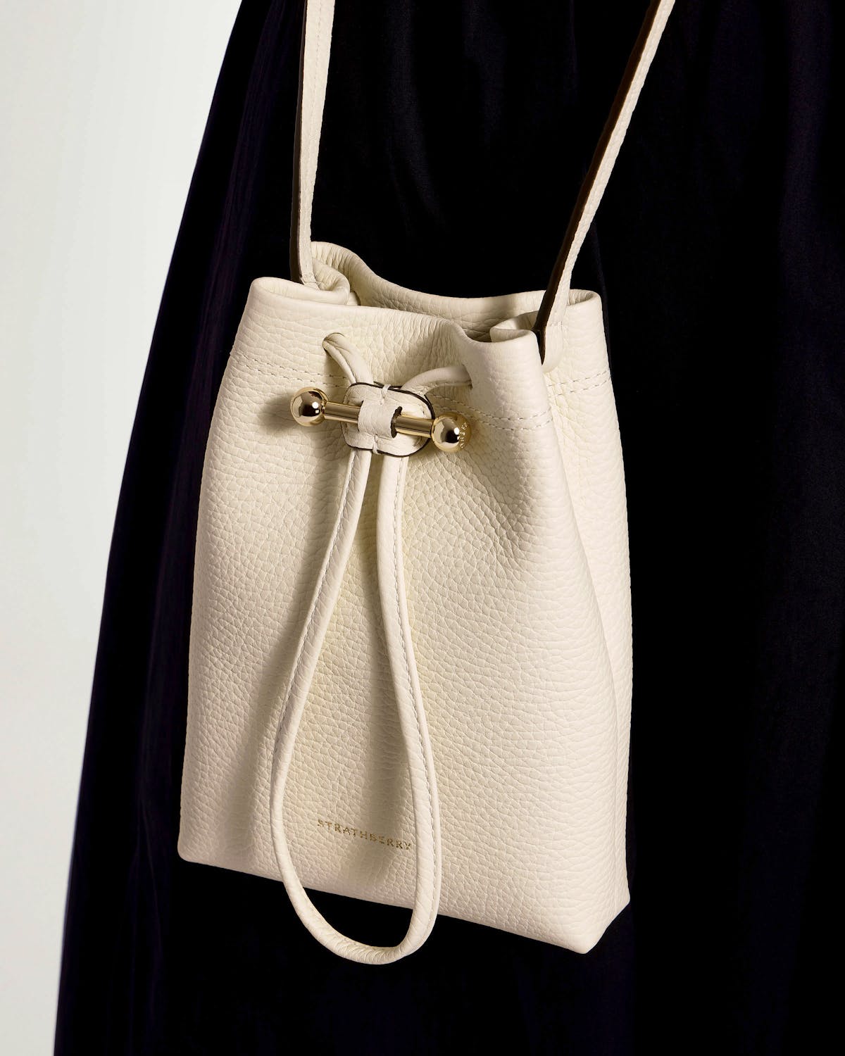 Vanilla pebbled leather Strathberry midi drawstring pouch with gold bar closure and strap.