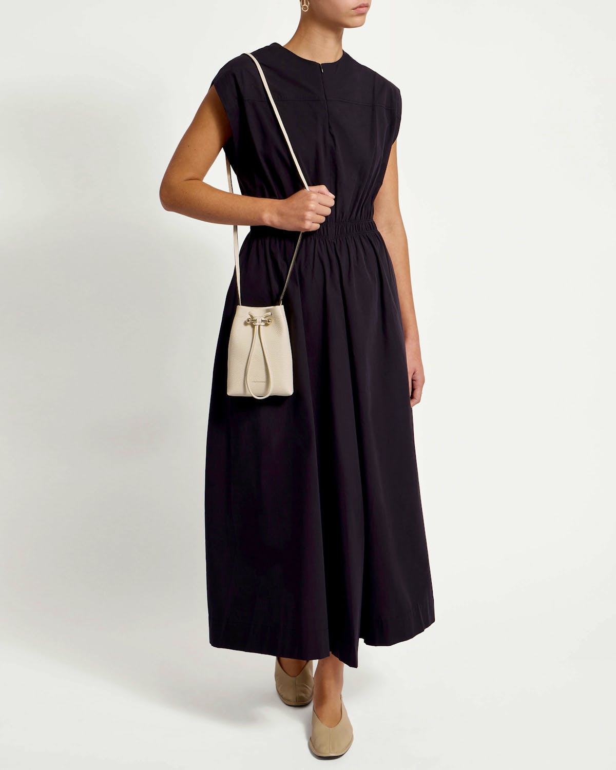 Model wearing a black dress and small vanilla leather drawstring pouch worn across the body.