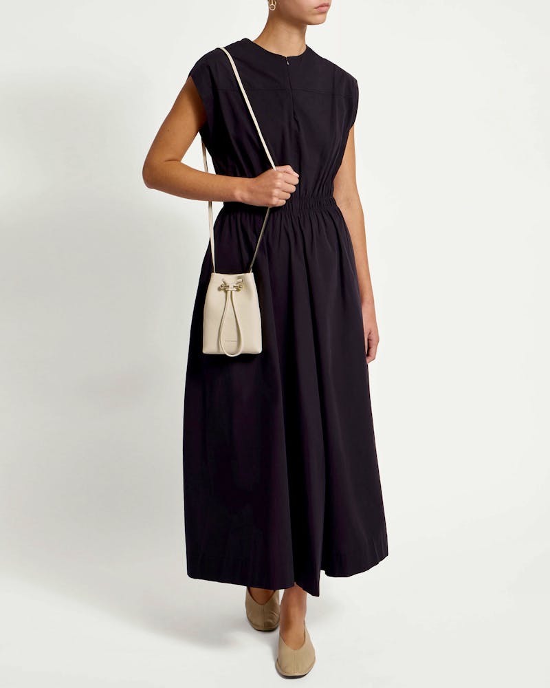 Model wearing a black dress and small vanilla leather drawstring pouch worn across the body.