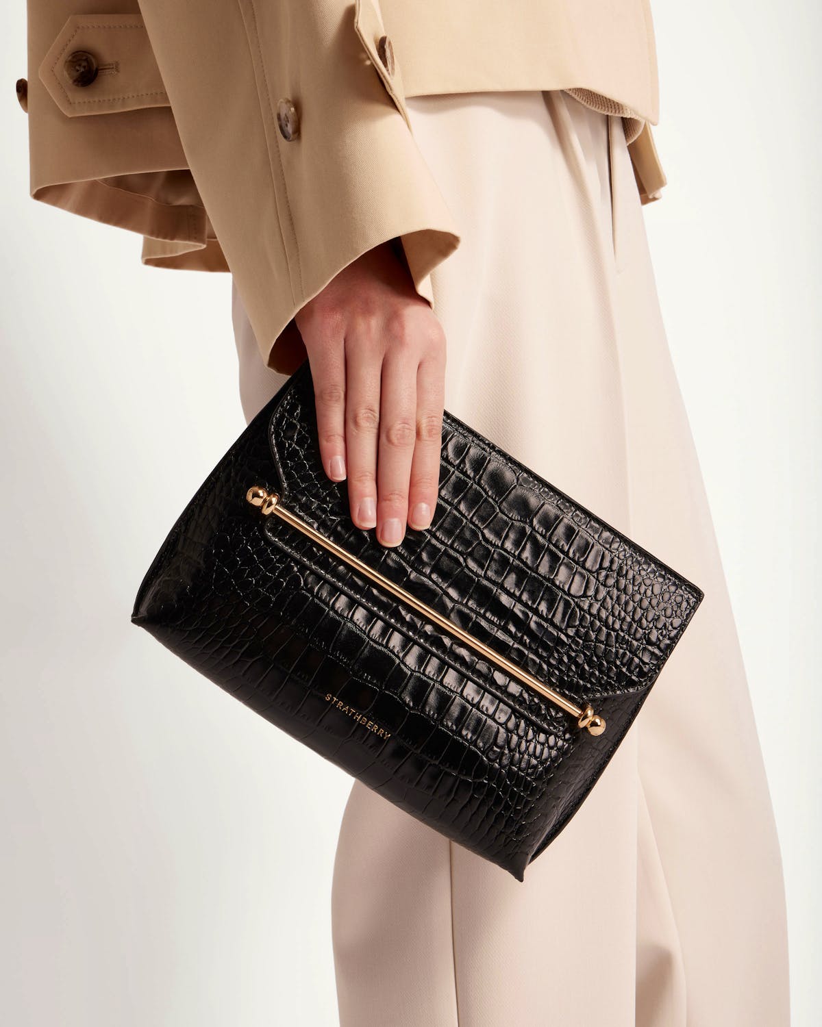 Handheld black croc-embossed Strathberry stylist clutch with gold bar detail.