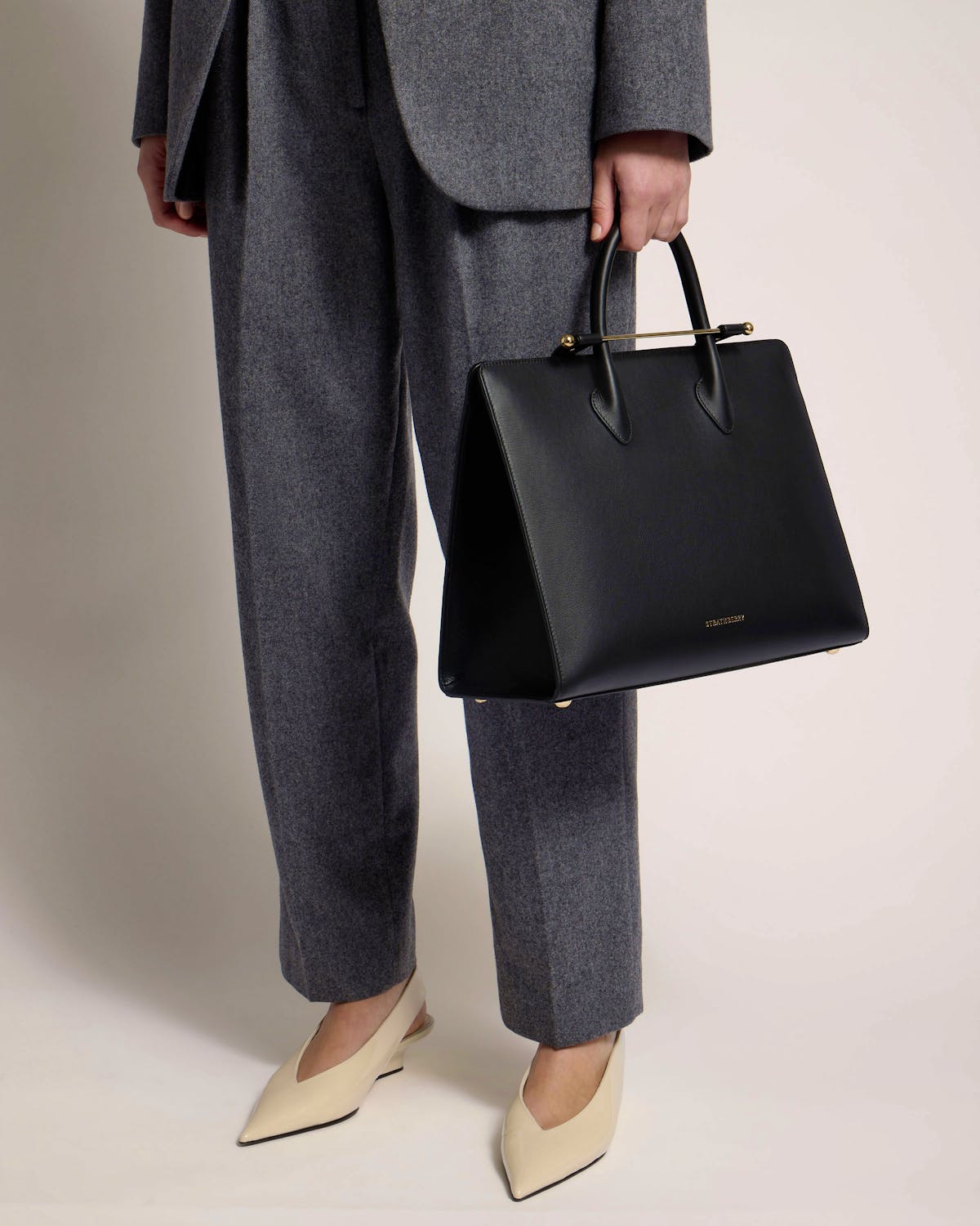 Black Strathberry leather tote held by top handles, model waist down.