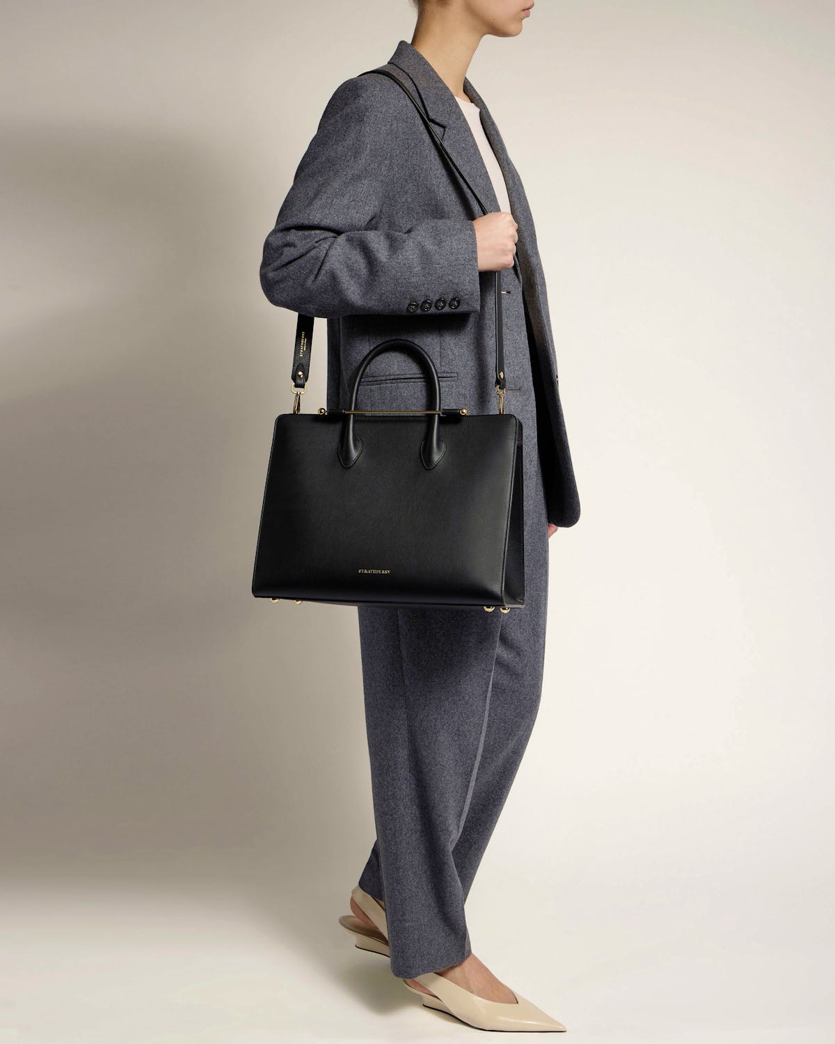 Woman in grey suit with black Strathberry tote worn on shoulder