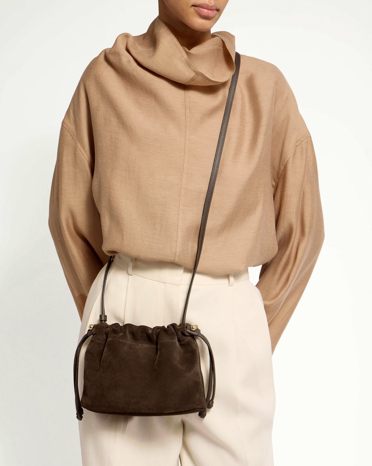 Chocolate suede drawstring bag worn crossbody on model, waist-up