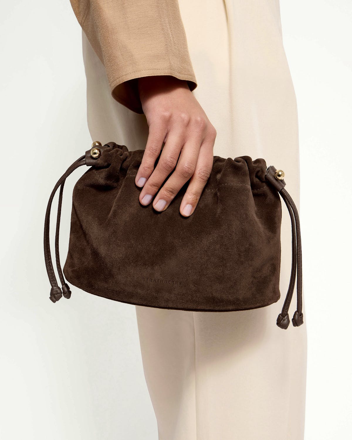 Strathberry Charlotte drawstring bag in chocolate suede held at hip