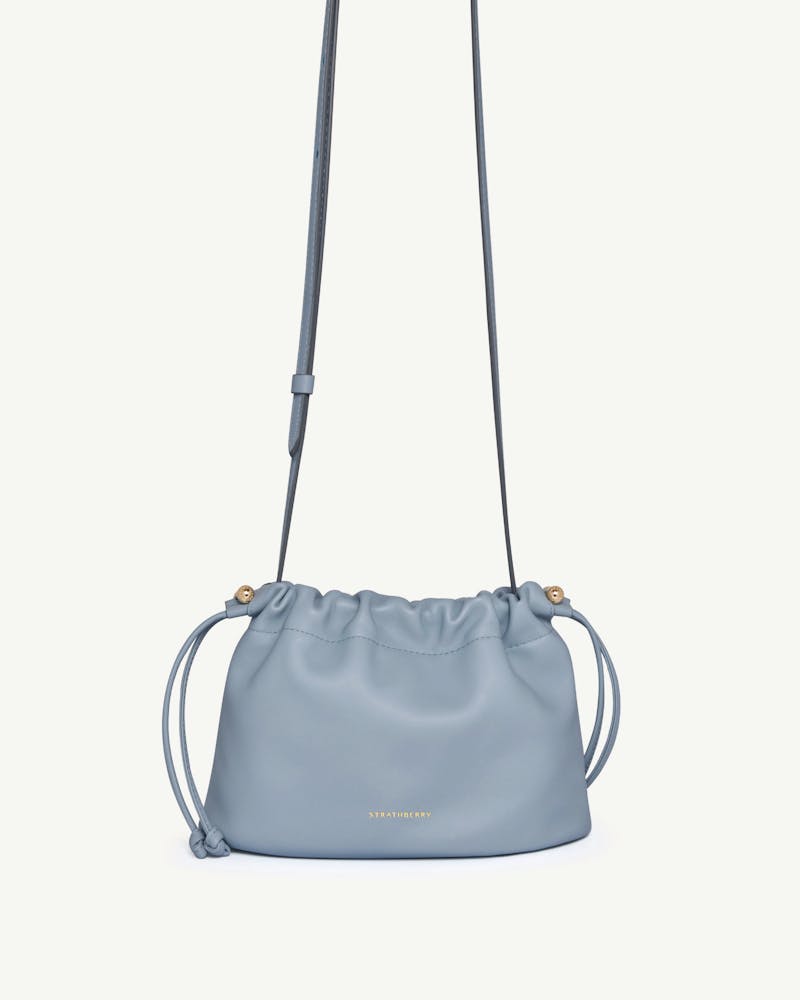 Dusky blue Charlotte drawstring bag with long strap and gold Strathberry logo.