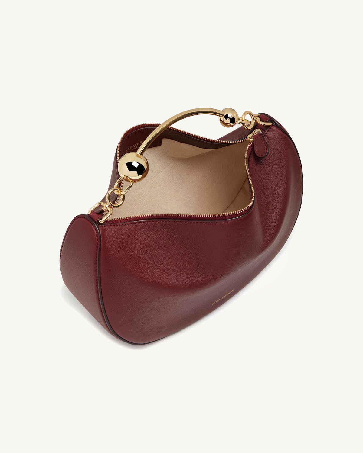 Oxblood leather crescent bag with gold curved top handle and beige interior.