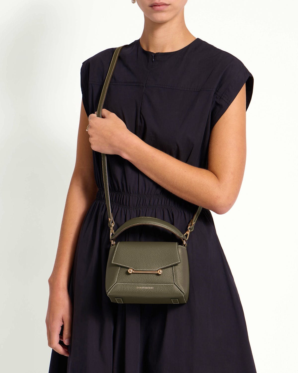 Model wearing Strathberry Mosaic Nano khaki leather bag with gold bar detail.