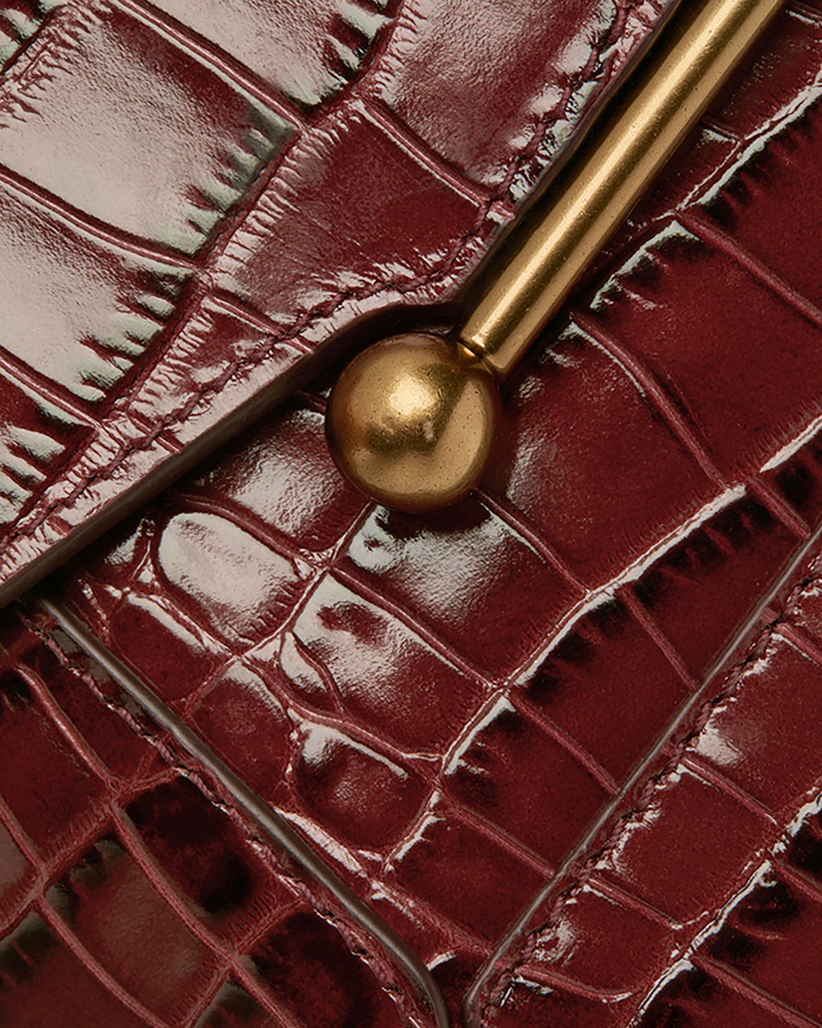 Close-up of burgundy croc leather bag front showing gold bar closure.
