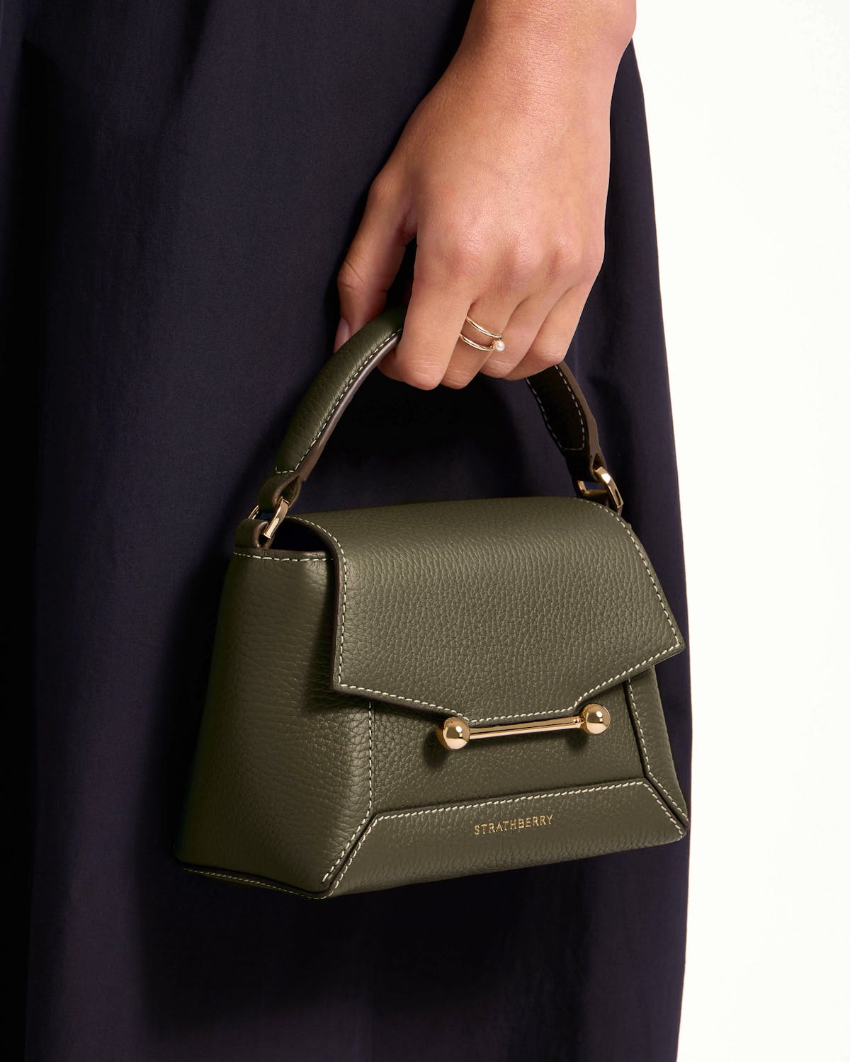 Hand holding khaki Mosaic Nano top-handle bag with gold bar and Strathberry logo.