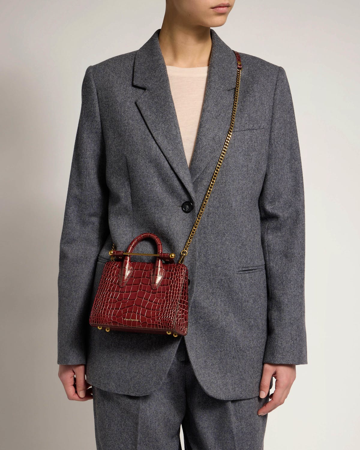 Strathberry croc-effect nano tote worn crossbody with gold chain strap.