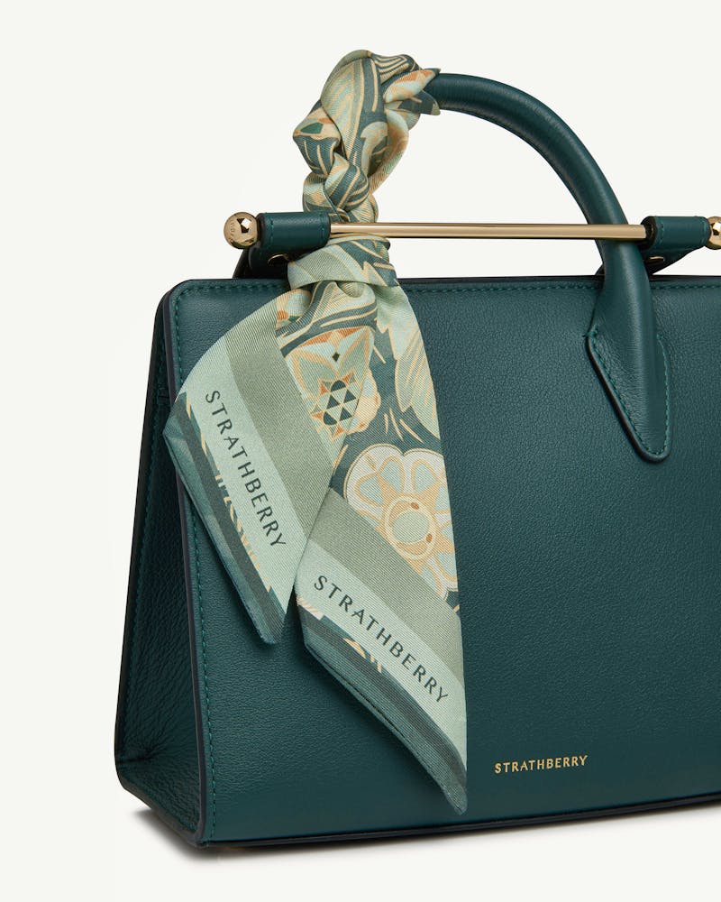 Silk skinny scarf in sage arcade print tied to Strathberry handbag handle.