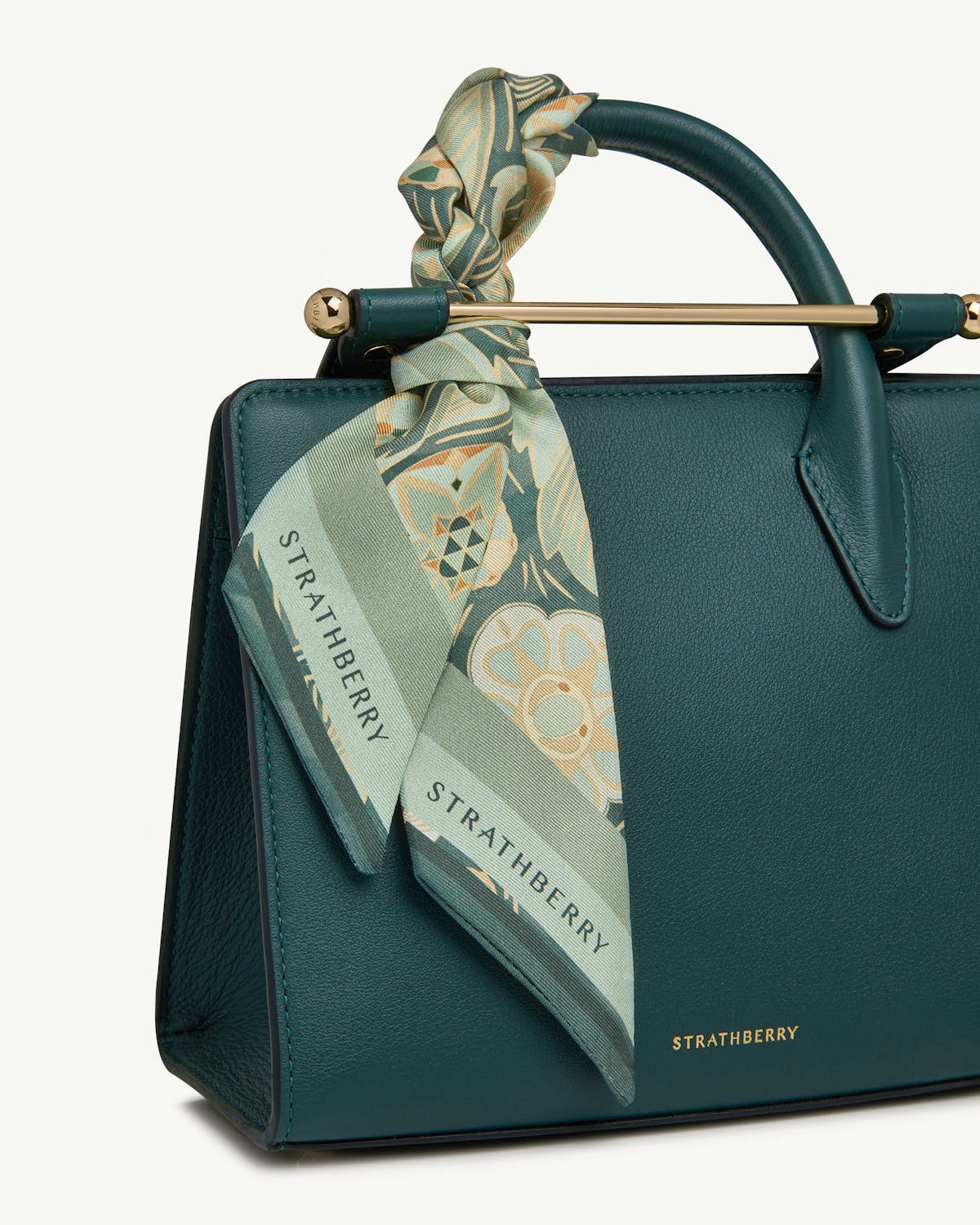 Silk skinny scarf in sage arcade print tied to Strathberry handbag handle.