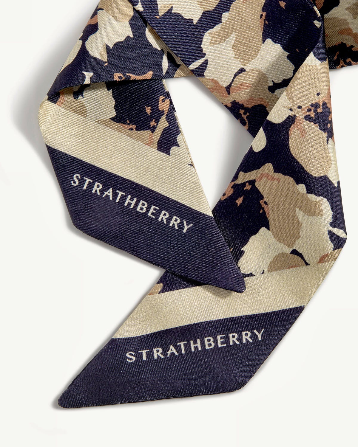 Navy and sand abstract floral skinny scarf with Strathberry logo, folded.