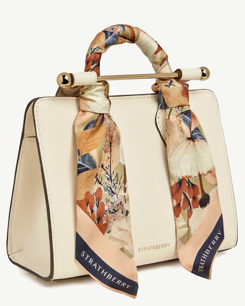 Silk skinny scarf in autumn floral print tied to cream Strathberry handbag handle.