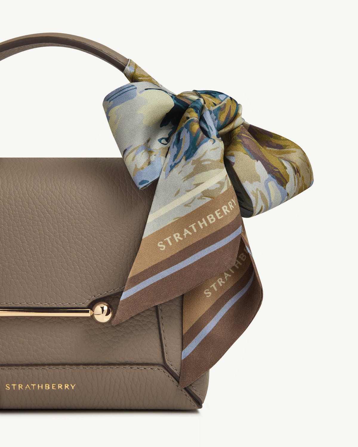 Strathberry silk skinny scarf in clay and blue abstract feather print tied to bag handle