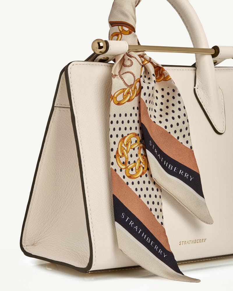 Black and tan chain-print silk skinny scarf tied to cream Strathberry bag handle