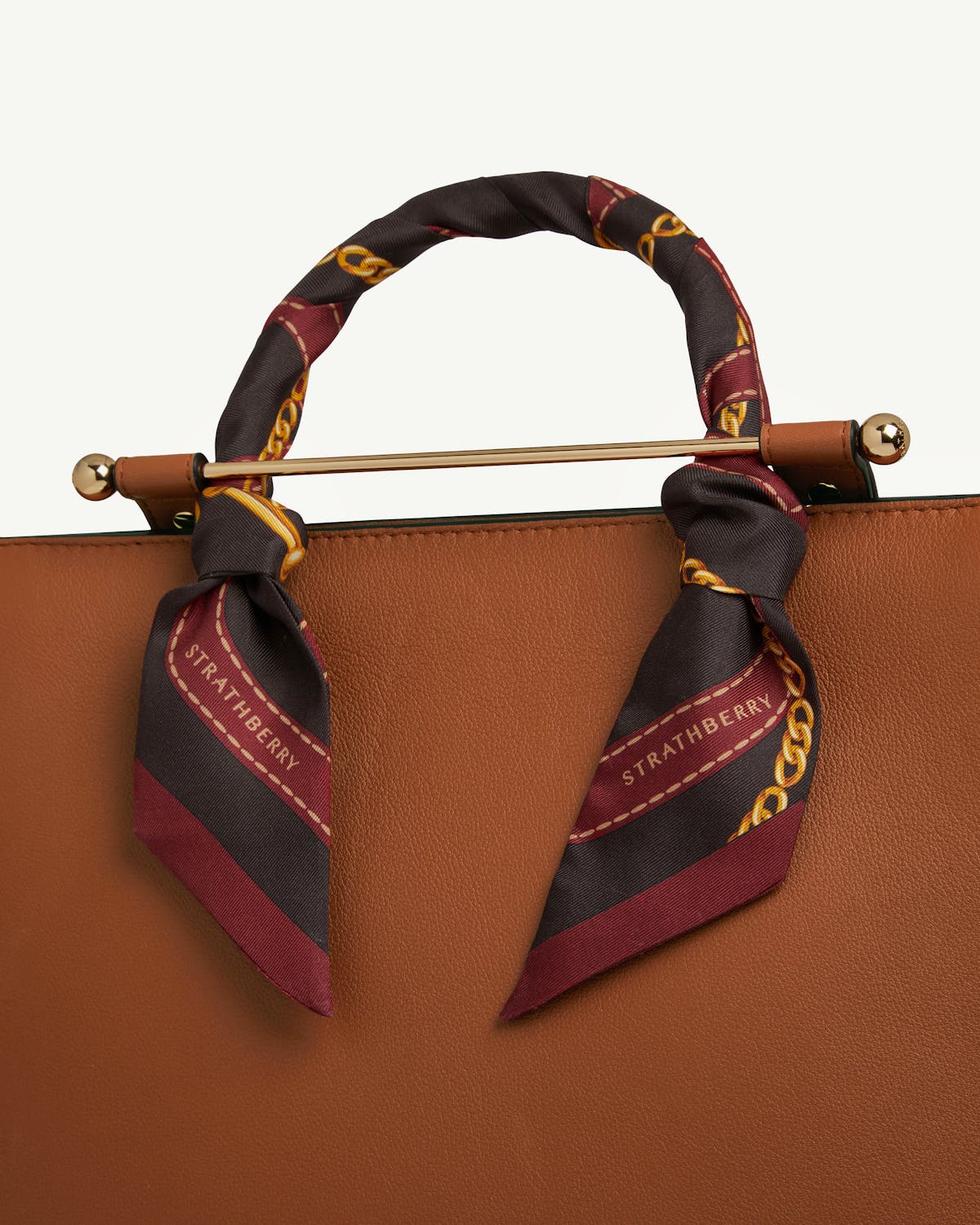 Oxblood and espresso silk skinny scarf tied around tan leather bag handle, Strathberry print.