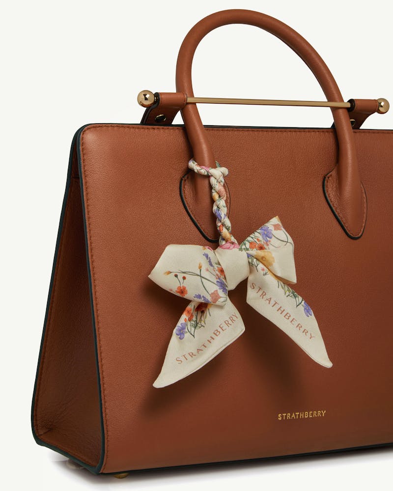 Brown leather handbag with vanilla floral silk skinny scarf tied to handle, Strathberry