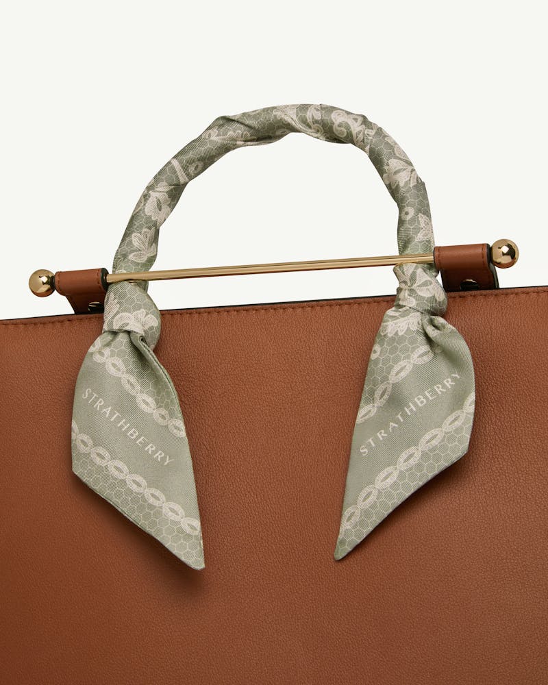 Sage silk skinny scarf with lace print tied around bag handle, Strathberry visible.