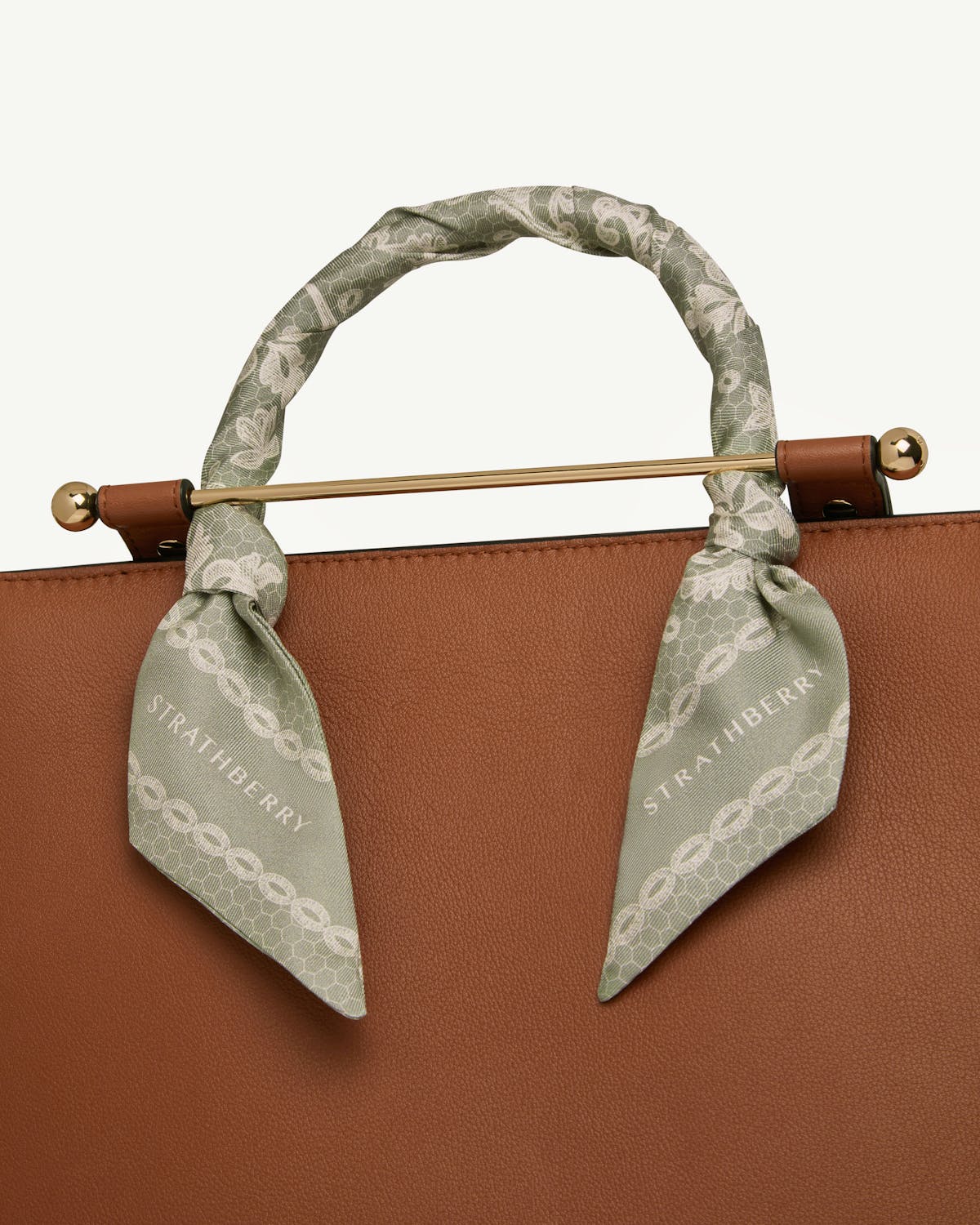 Sage silk skinny scarf with lace print tied around bag handle, Strathberry visible.