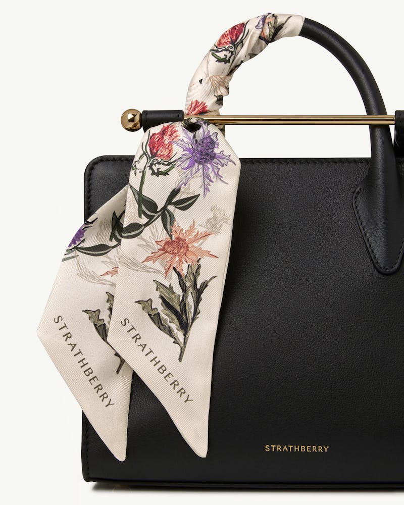 Silk skinny scarf in vanilla with forest green thistle print tied to Strathberry bag.