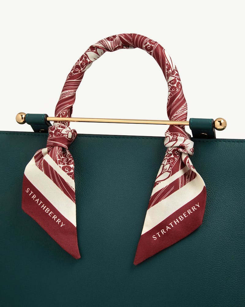 Oxblood wallpaper print silk skinny scarf tied to bag handle with Strathberry logo.