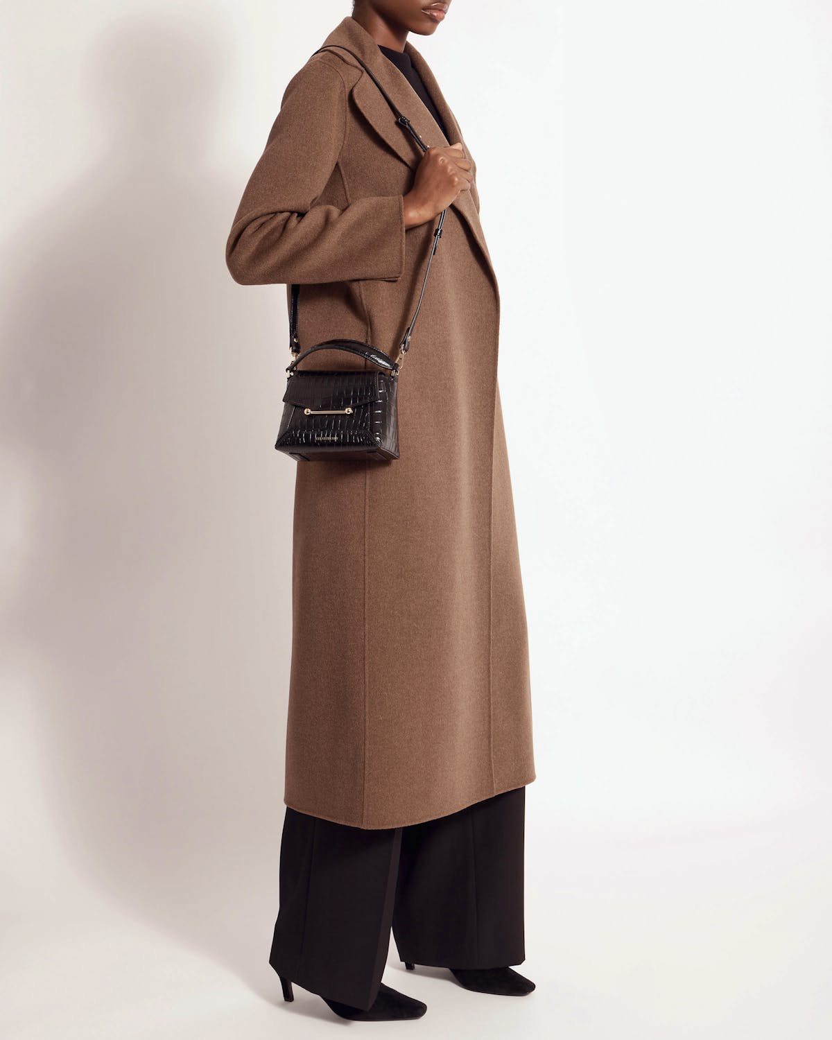 Model standing wearing a black croc-embossed small top-handle bag crossbody