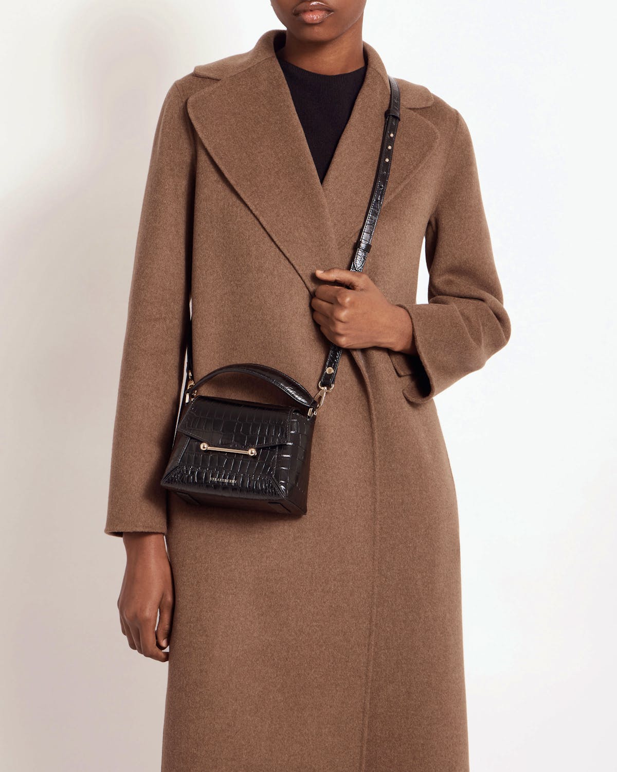Strathberry Soft Croc Mosaic Nano crossbody bag worn over brown coat.