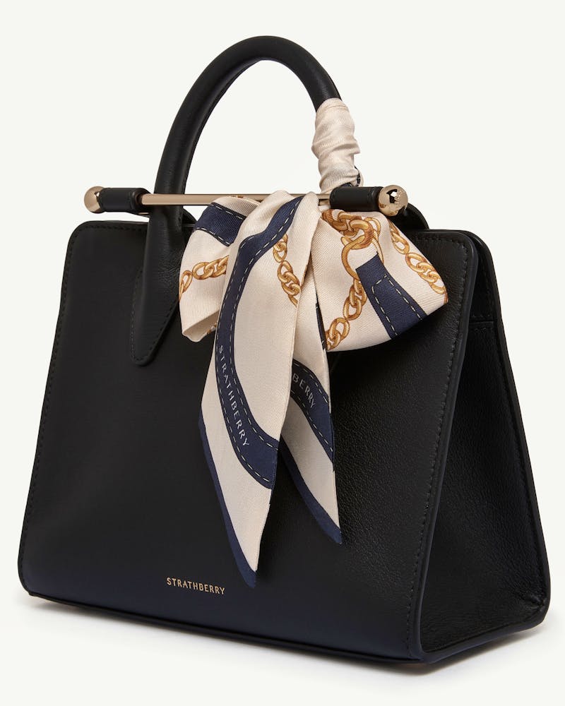 Black Strathberry bag with navy and vanilla belt-print silk skinny scarf tied to handle