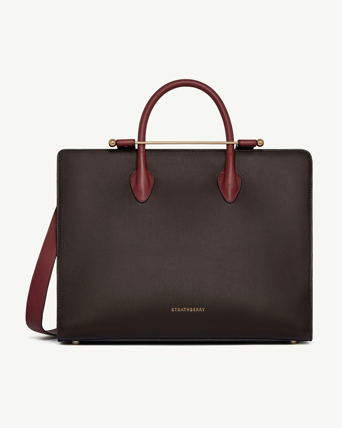 Strathberry tote in espresso with oxblood handles and gold bar detail.