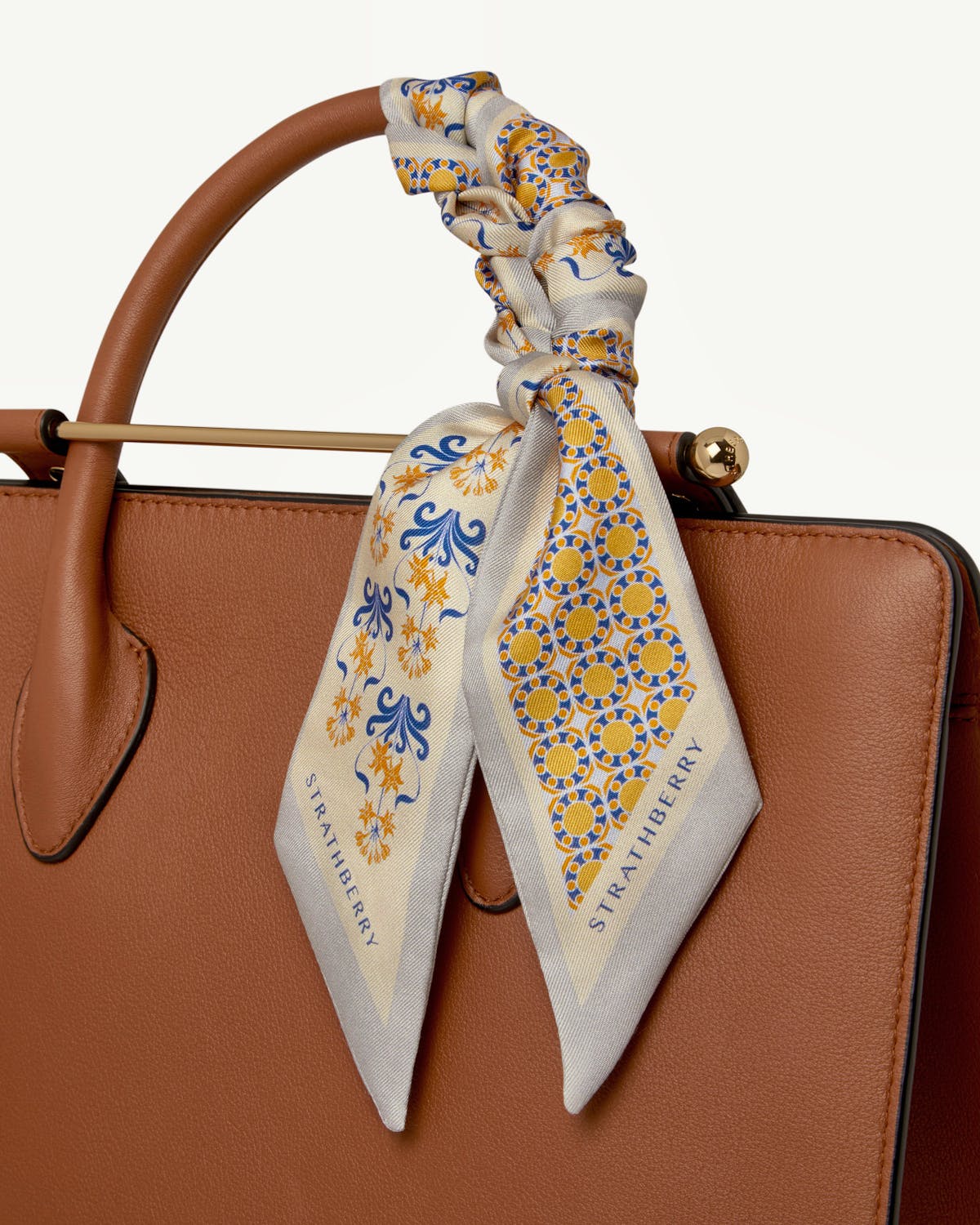 Silk skinny scarf in marble grey and brûlée geometric tile tied to Strathberry bag.