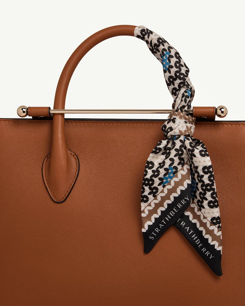Silk skinny scarf tied to chestnut leather bag handle, Fair Isle pattern, Strathberry logo visible.