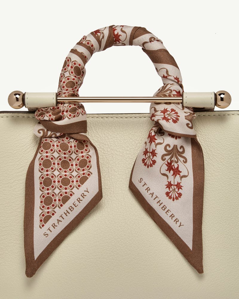 Tan geometric skinny silk scarf tied around bag handle with Strathberry logo.