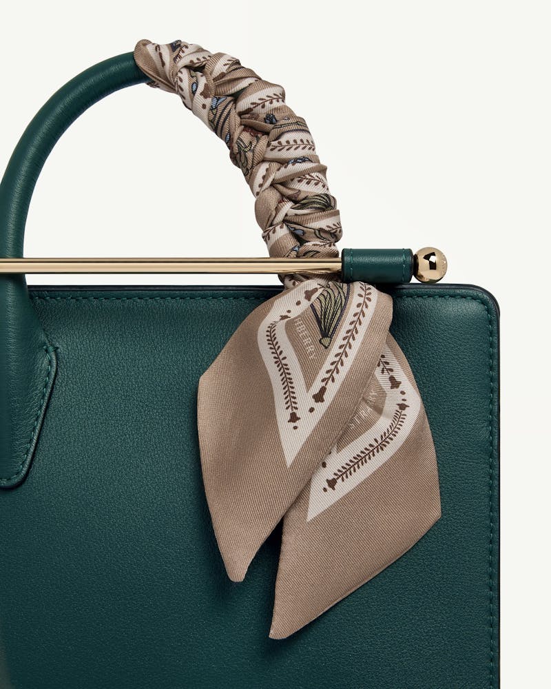 Silk skinny scarf in geometric caramel tied around green leather bag handle.