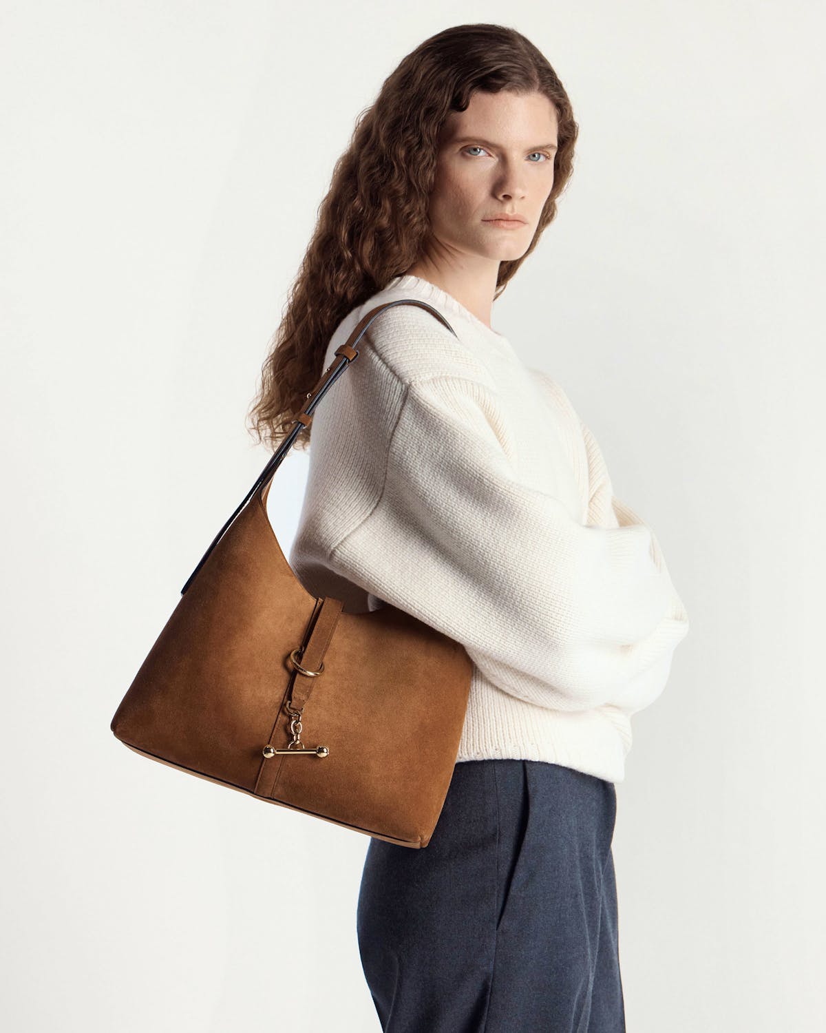 Model wearing white sweater and trousers carrying tan suede Kite Hobo shoulder bag.