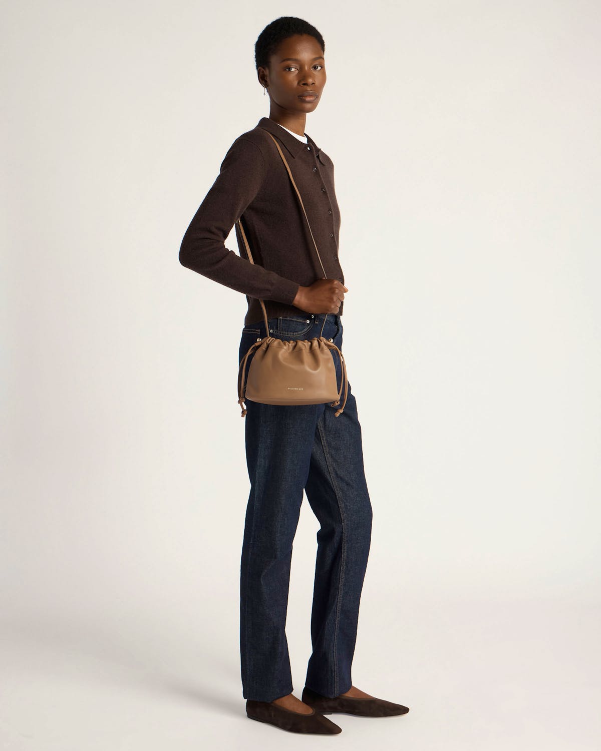 Model in dark cardigan and jeans carrying clay drawstring bag crossbody