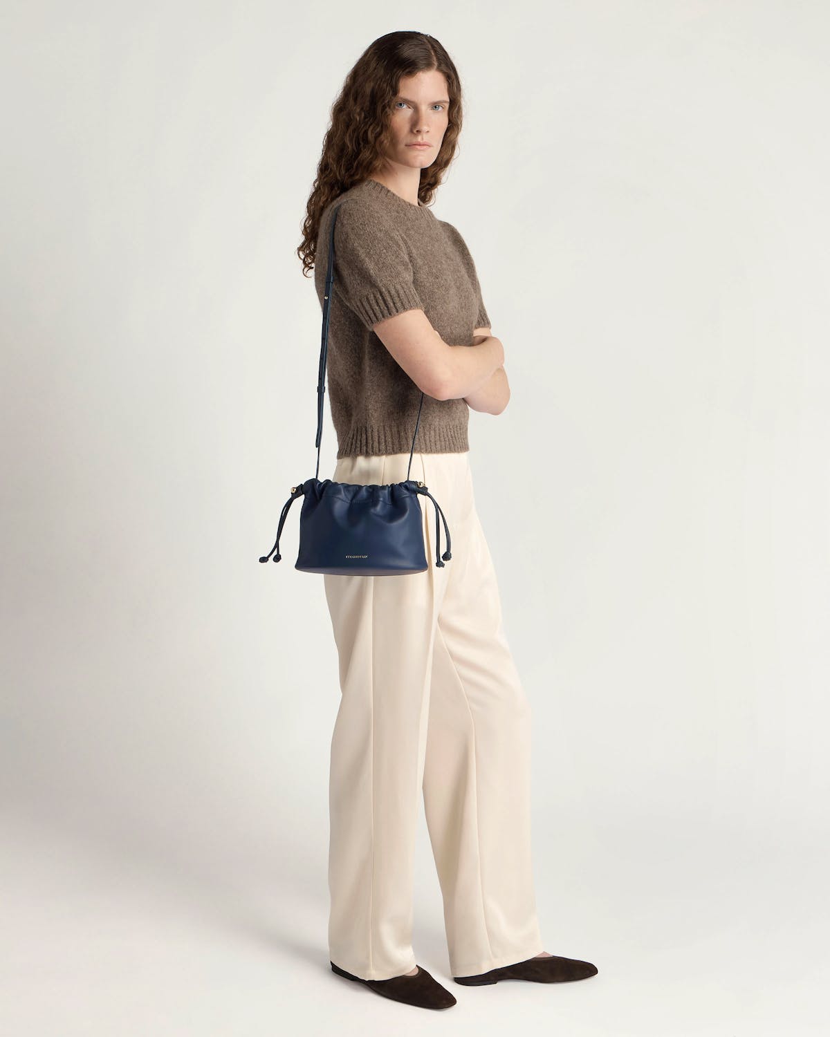 Model standing wearing a marine blue drawstring bag over shoulder in studio.