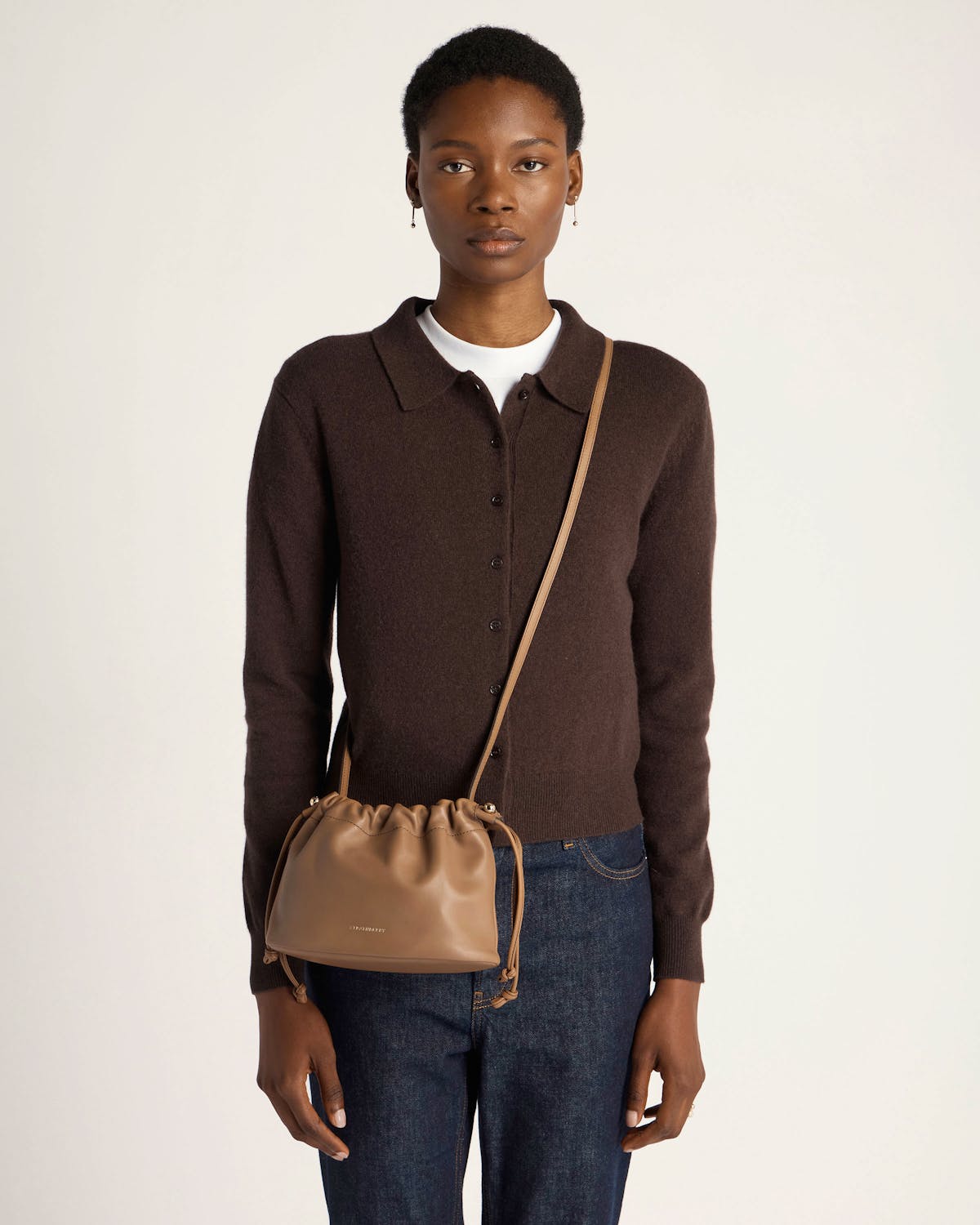 Model wearing a clay Charlotte drawstring bag with knotted side ties, across body.