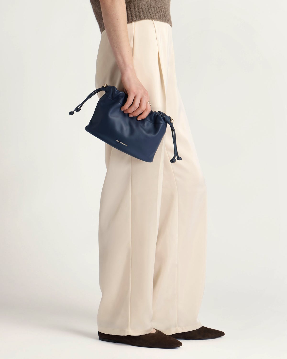 Model holding Strathberry Charlotte drawstring bag in marine blue at hip.