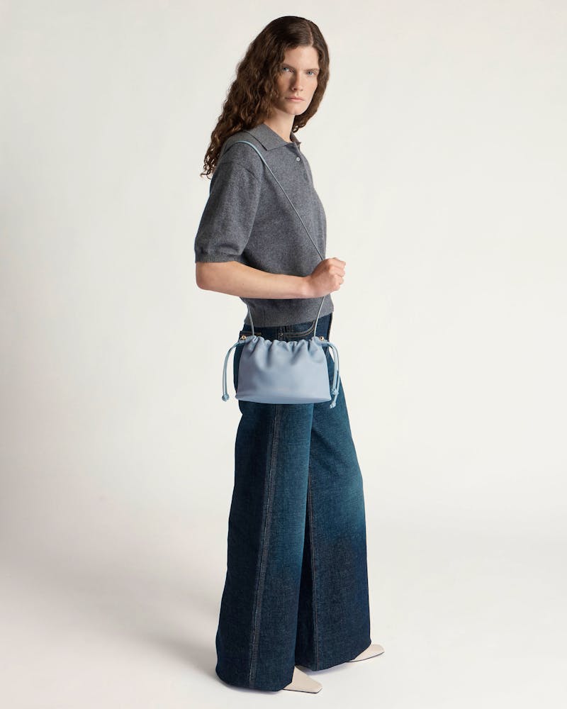 Model wearing dusky blue Charlotte drawstring bag worn across body at hip.