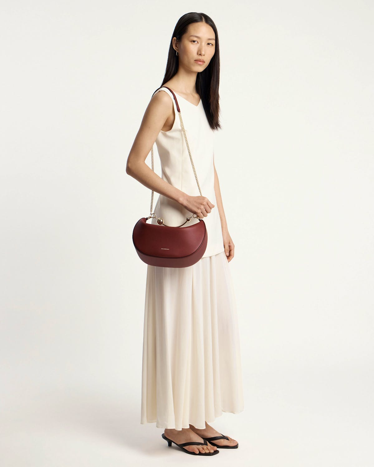 Woman in white dress carrying oxblood crescent moon bag with chain strap