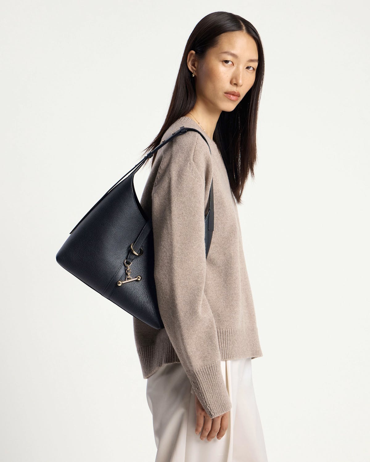 Model wearing a black hobo shoulder bag, beige jumper and white trousers.