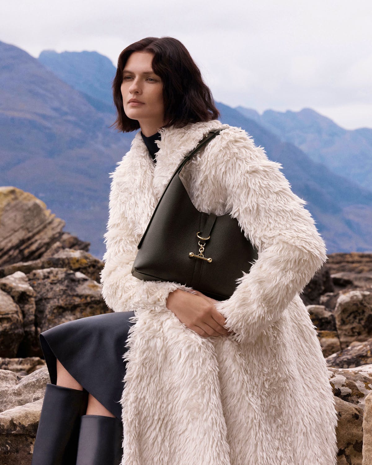 Model wearing cream faux-fur coat holding espresso Kite hobo bag with gold hardware.