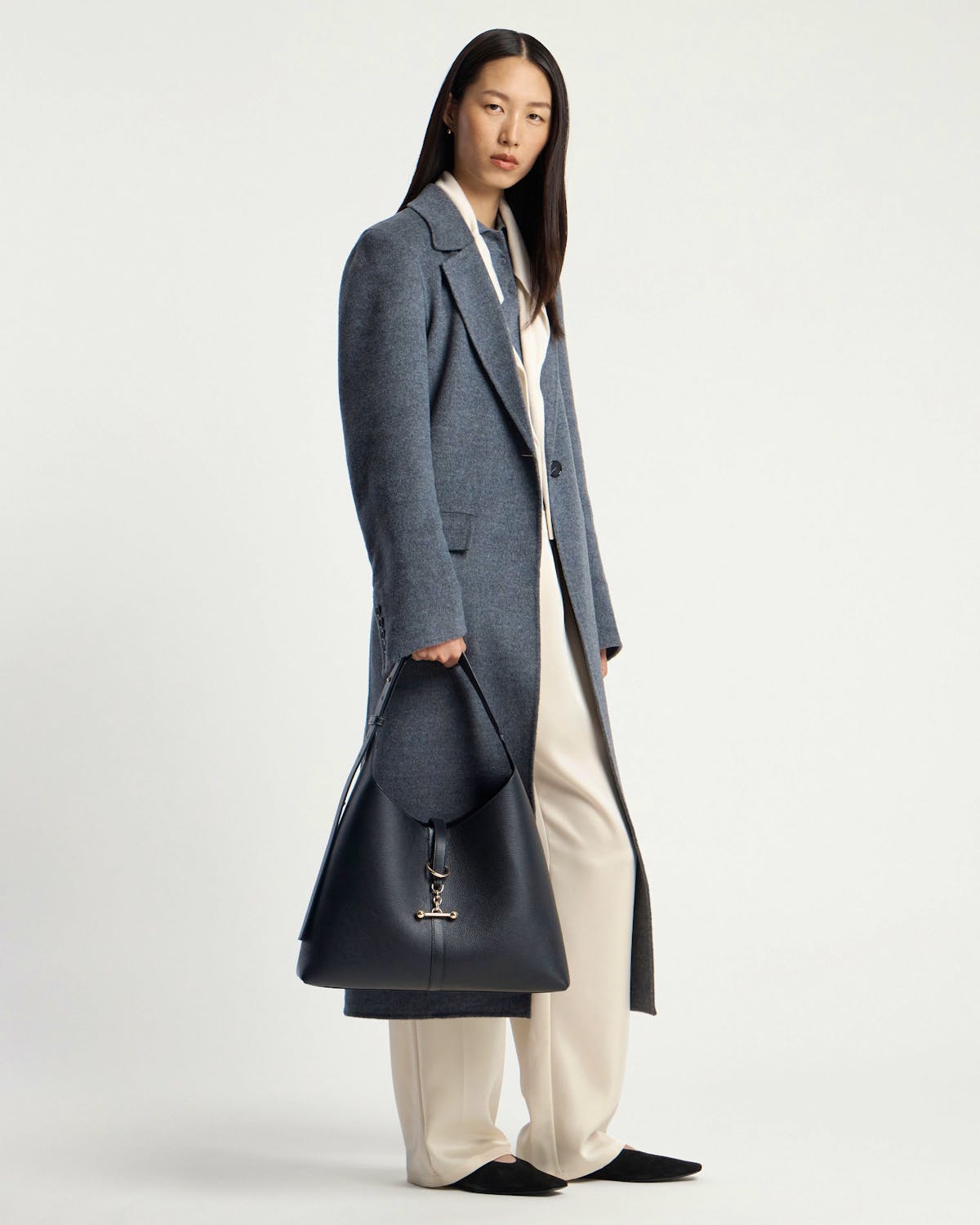 Woman in a grey coat holding a black hobo bag with gold hardware.