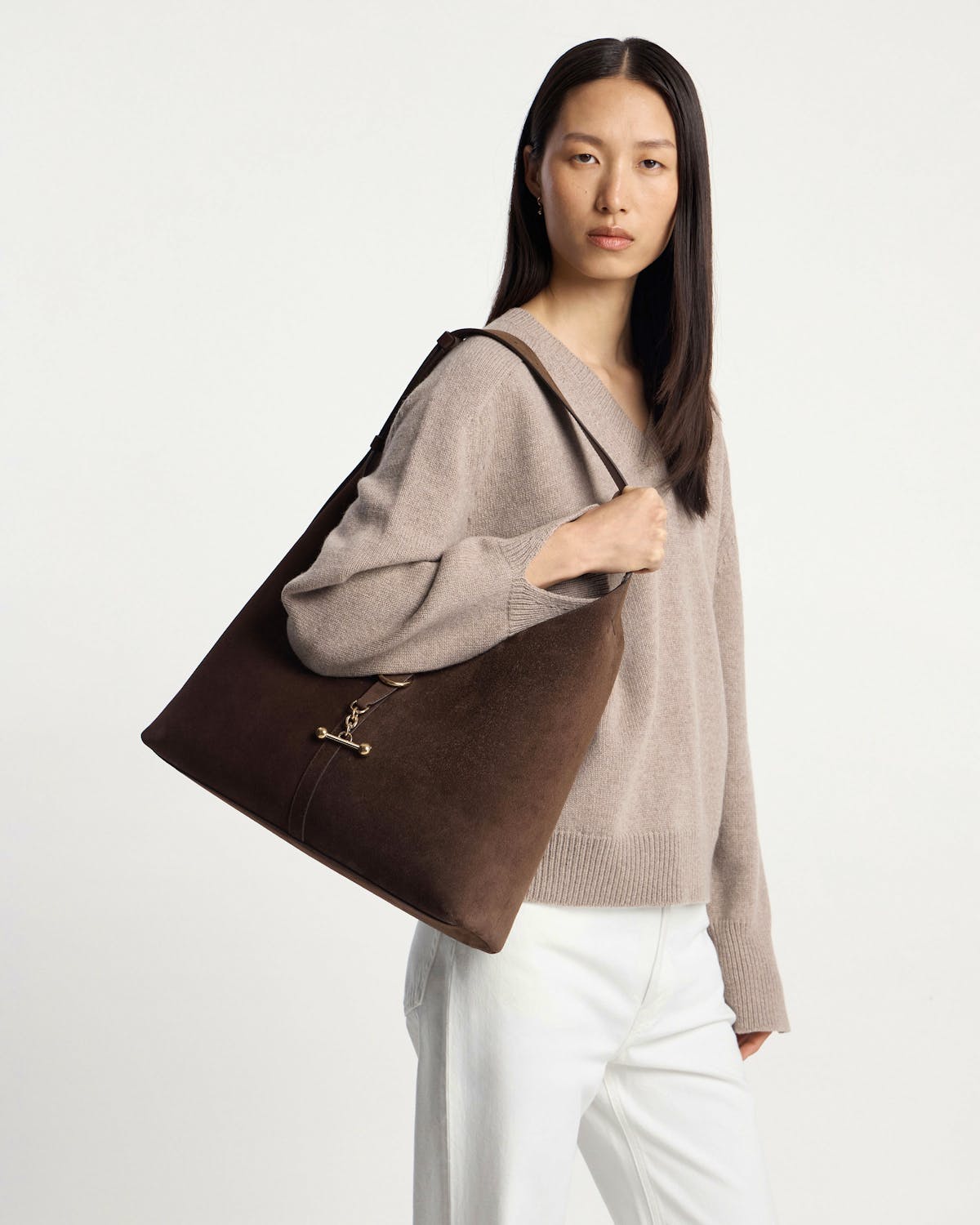 Model carrying chocolate suede Kite Hobo Maxi shoulder bag with gold clasp.