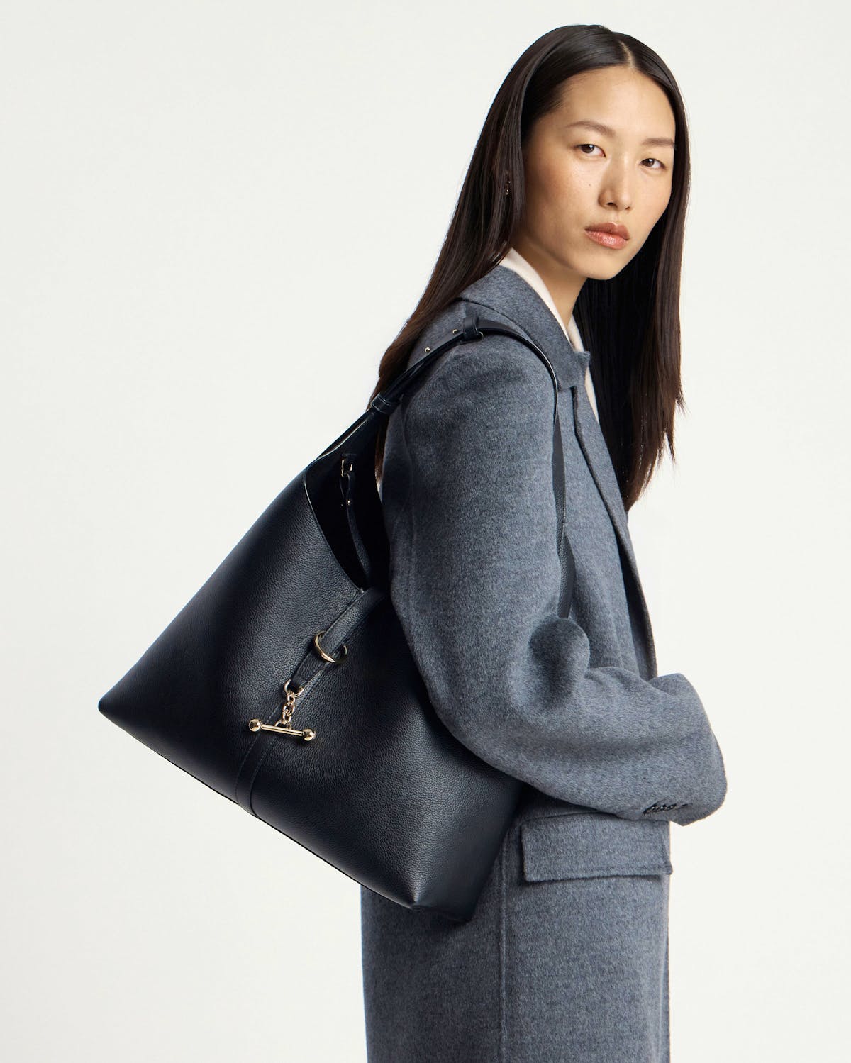 Model wearing a black hobo bag with gold hardware over shoulder.