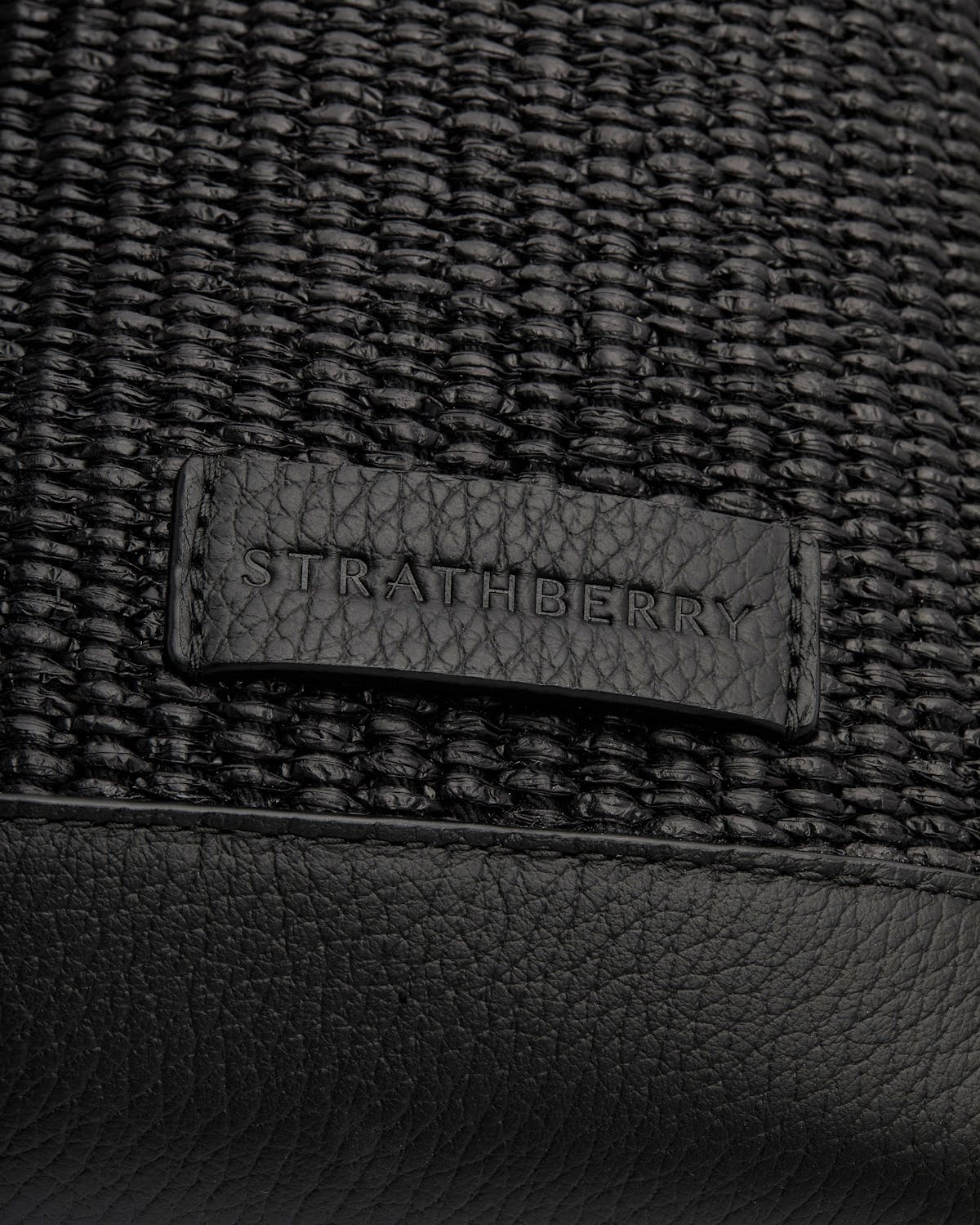 Black raffia weave with leather patch embossed Strathberry and pebbled leather trim.